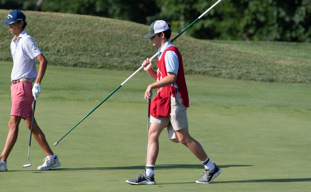 A young caddie holds the flagstick at the 2024 MGA Junior Championship